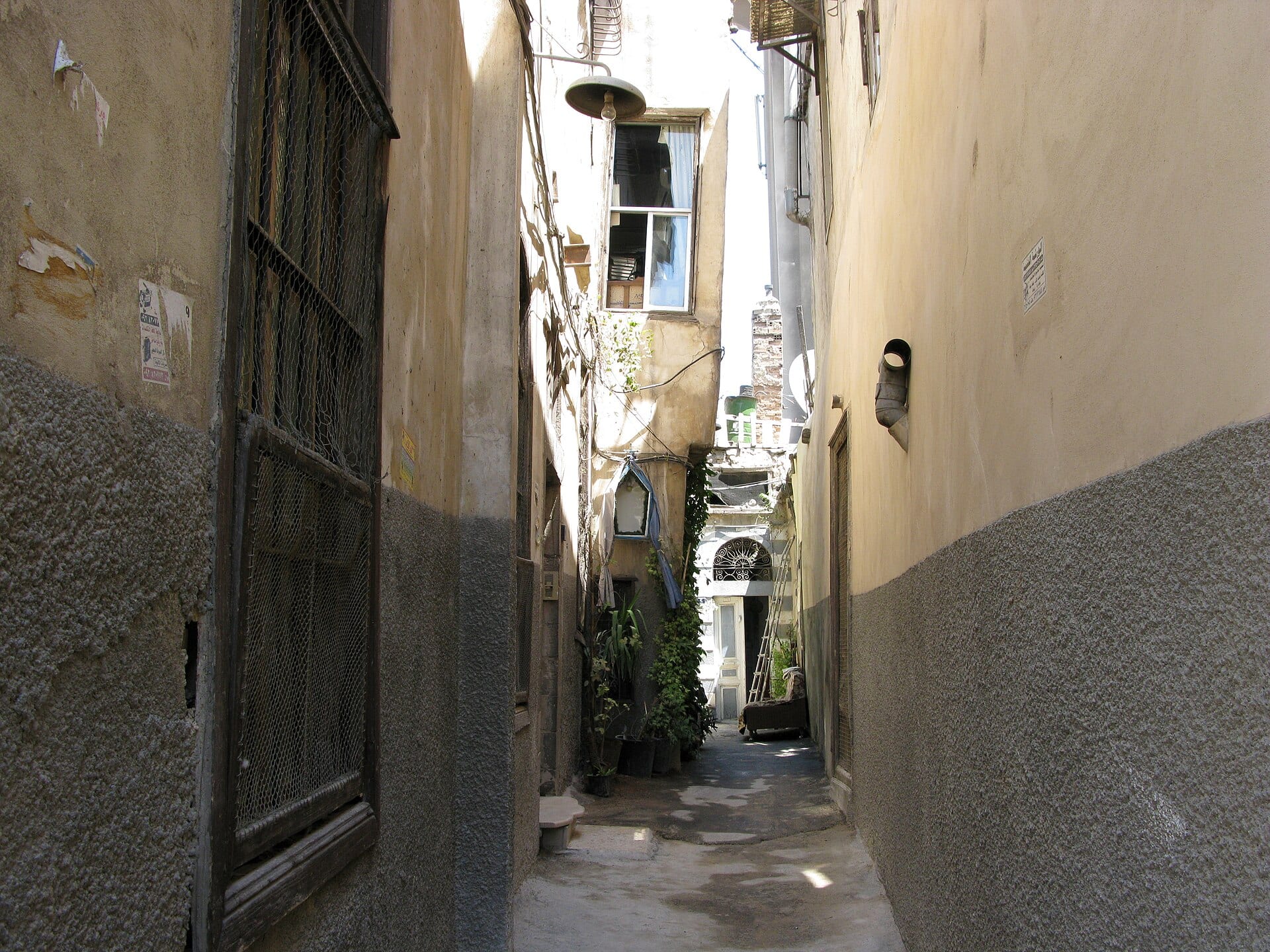 A narrow stone alleyway in old Damascus, upper storeys leaning towards each other overhead.