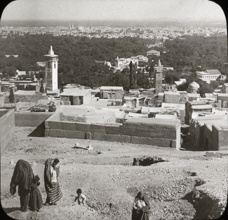 A distant historical view of Damascus, the city low on the plain beneath a wide sky.