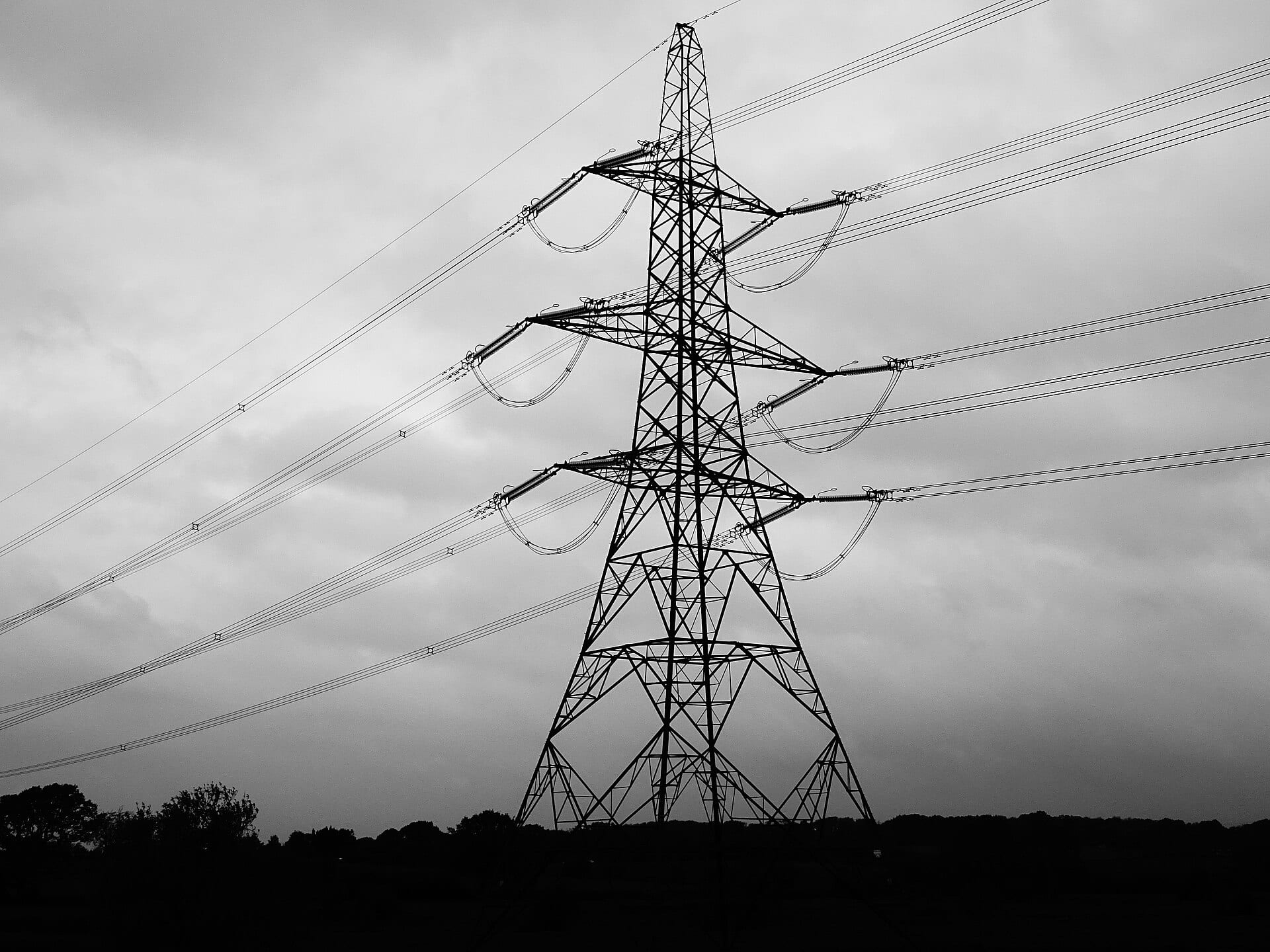 A lattice tower in silhouette against a grey sky, its conductors anchored in tension strings that loop back on themselves.