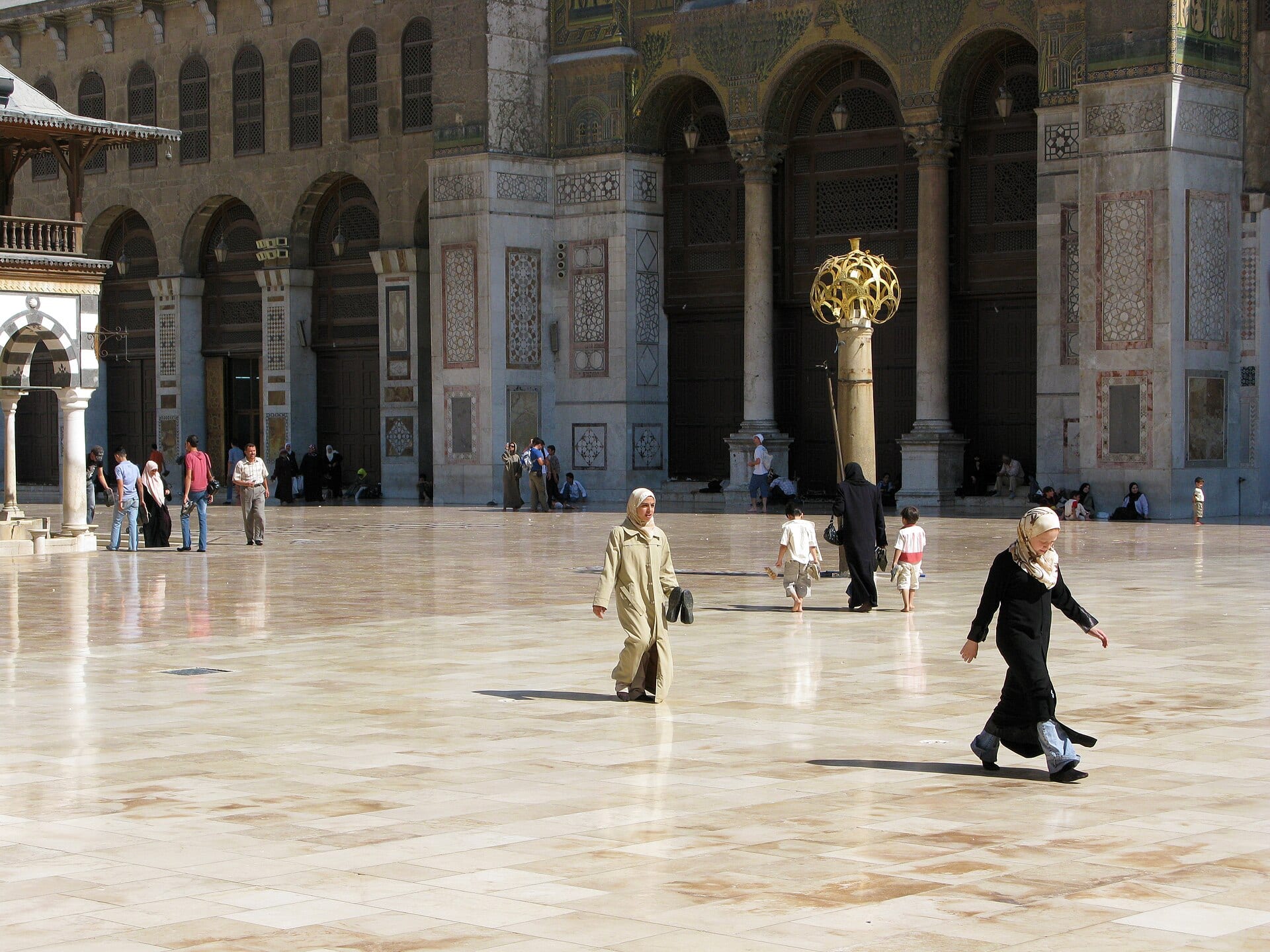 The courtyard of the Umayyad Mosque in Damascus, its arcades and mosaic-faced walls in flat daylight.